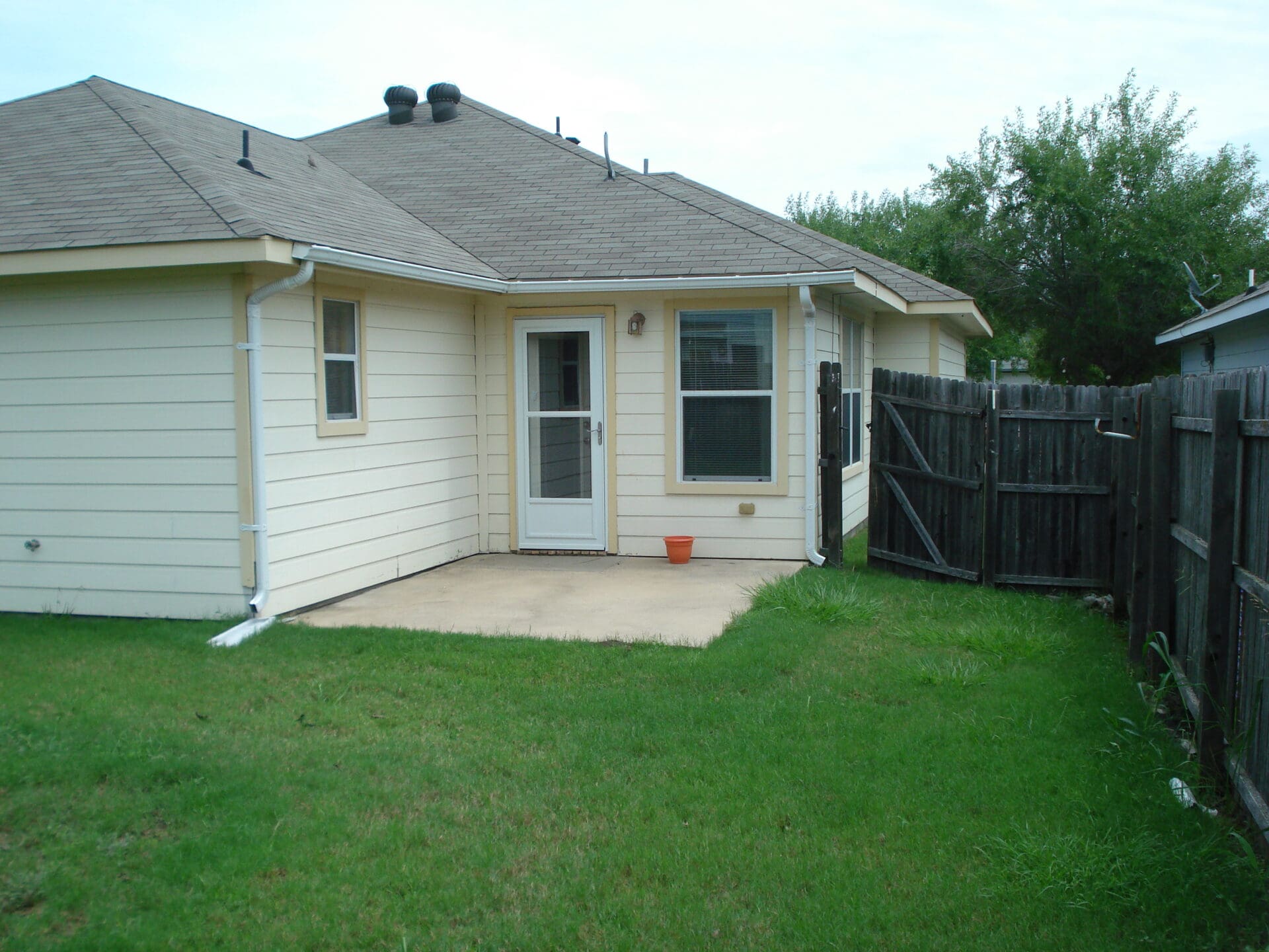 Backyard of a suburban house with green lawn and fenced area.
