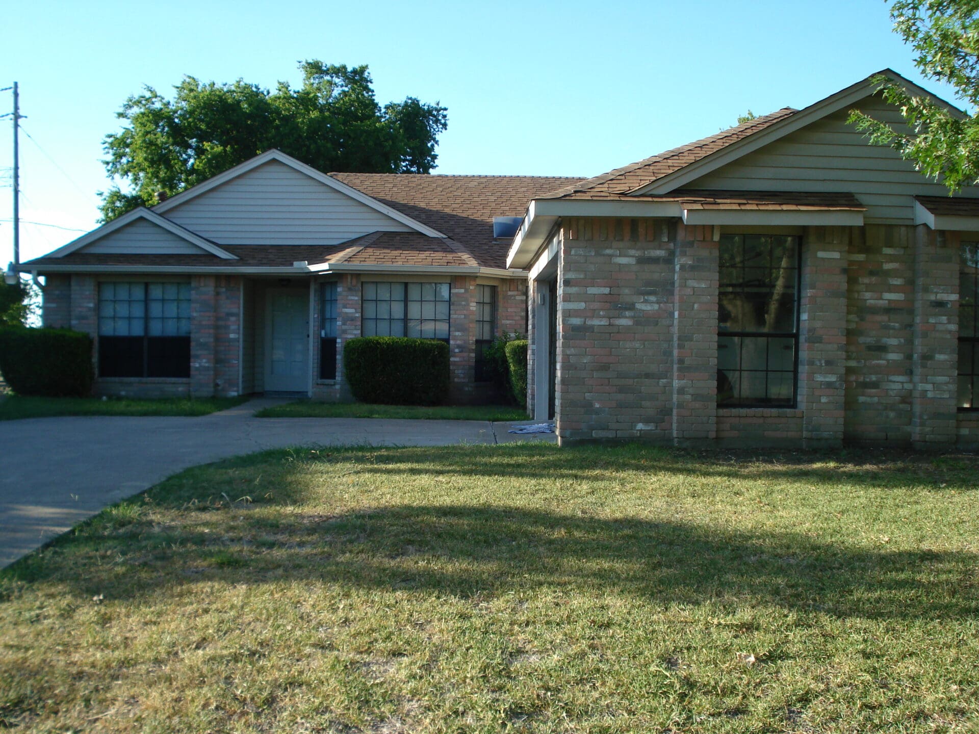 Single-story brick house with a large front lawn under clear skies.
