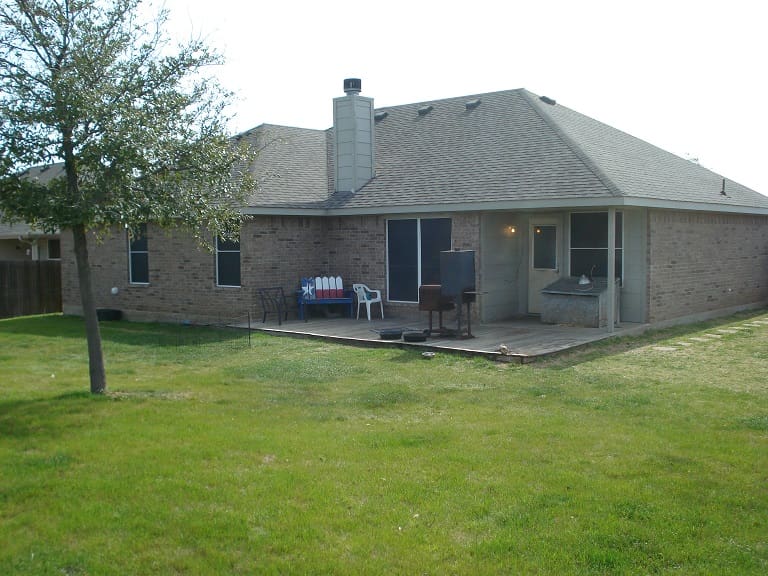 Backyard of a brick house with a covered patio and green lawn.