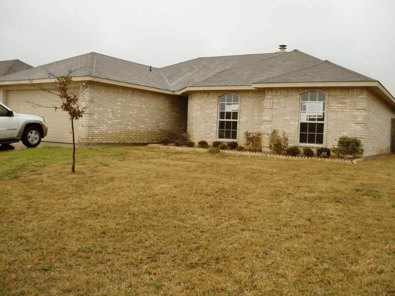 A single-story brick house with a large front yard and a small tree.