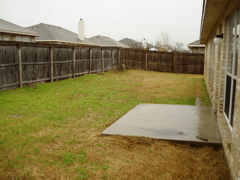 Empty backyard with grass and a concrete patio.