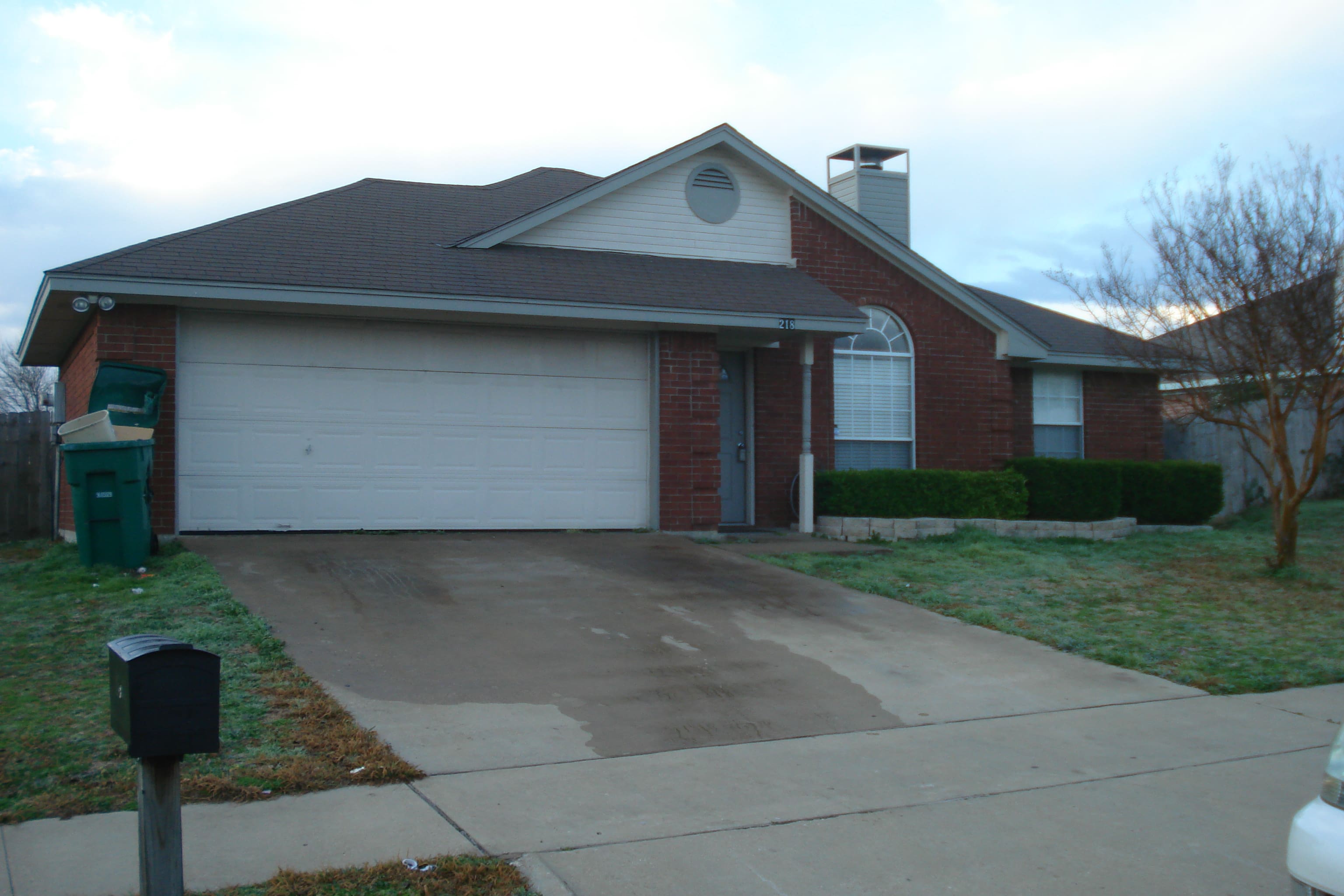 A single-story brick house with a two-car garage and a sloped driveway.