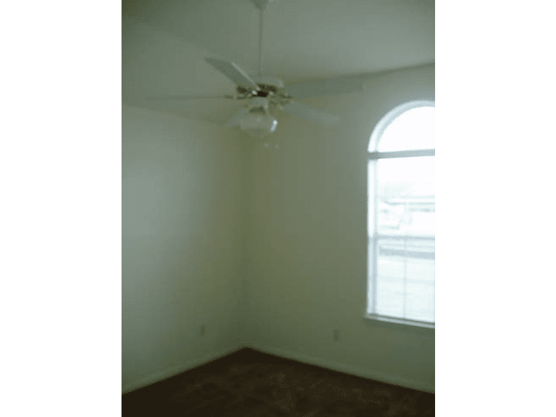 Empty corner of a room with a window and ceiling fan.
