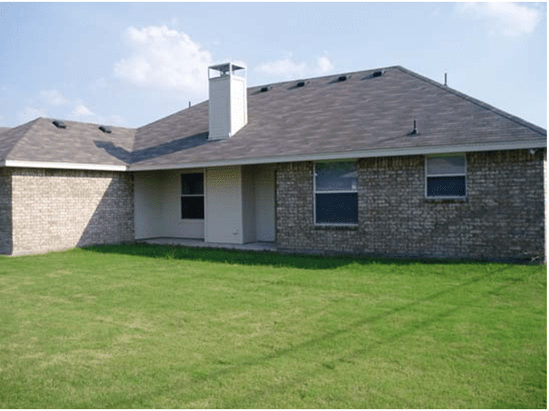 Back view of a brick house with a sloped roof and a spacious green lawn.