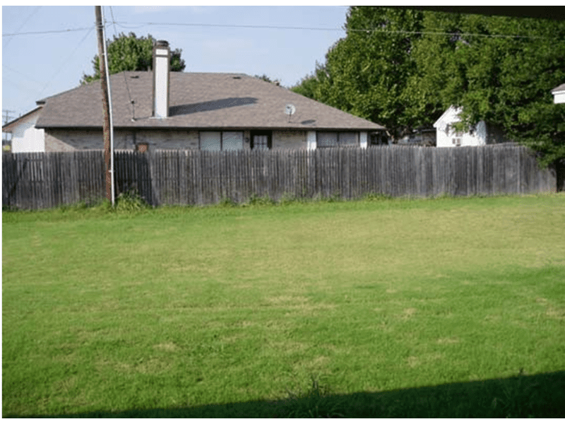 A green grassy field with a wooden fence and houses in the background.