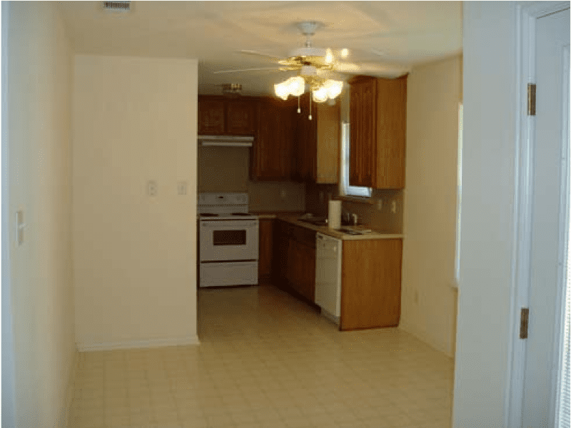 Empty kitchen with wooden cabinets, white appliances, and a ceiling fan light.