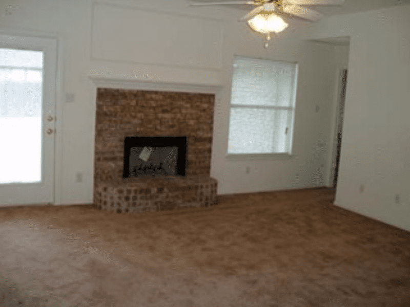 Empty room with brown carpet and brick fireplace.