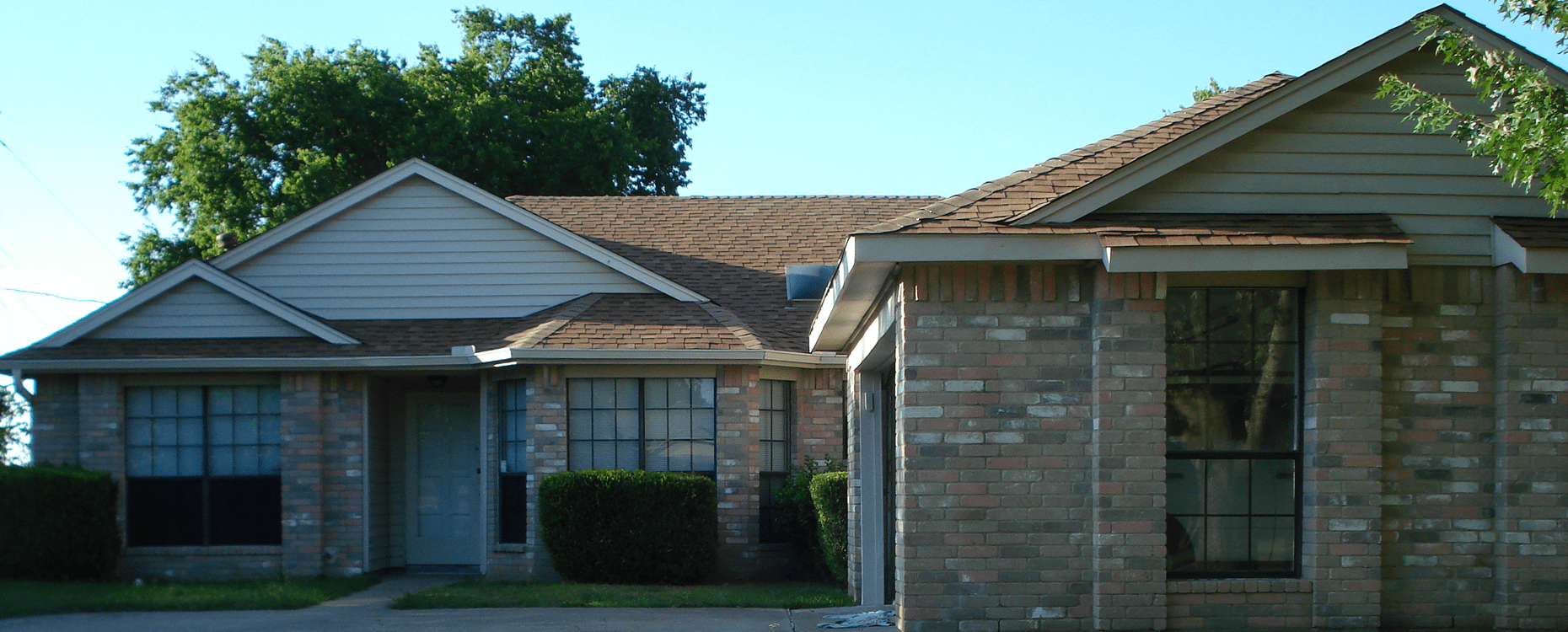 Suburban houses with brick walls and manicured bushes under a clear blue sky.