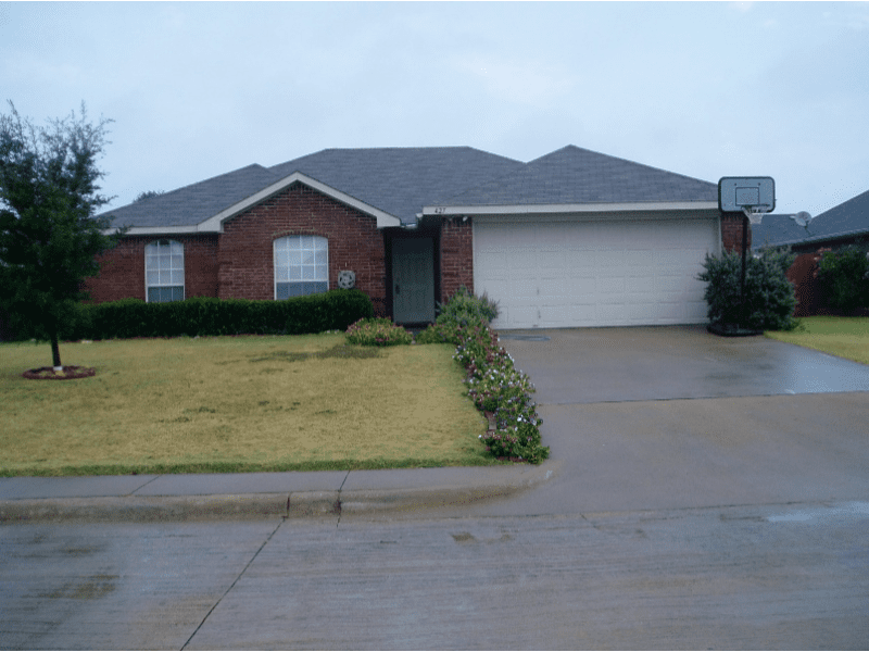 A single-story brick house with a two-car garage and a basketball hoop.
