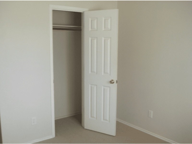 Empty room with an open white closet door and beige walls.