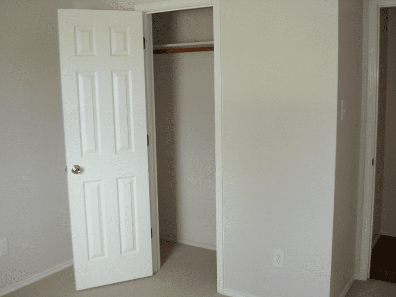 Empty closet with open door in a plain room.