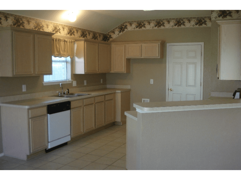 Empty kitchen with wooden cabinets and tiled floor.