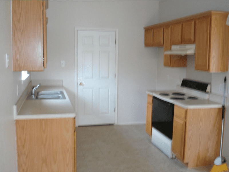 Empty kitchen with wooden cabinets, white appliances, and a door.