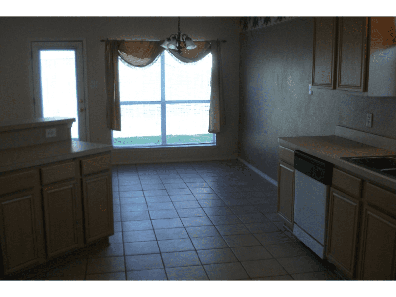 Empty kitchen with tiled floor and large window seating area.