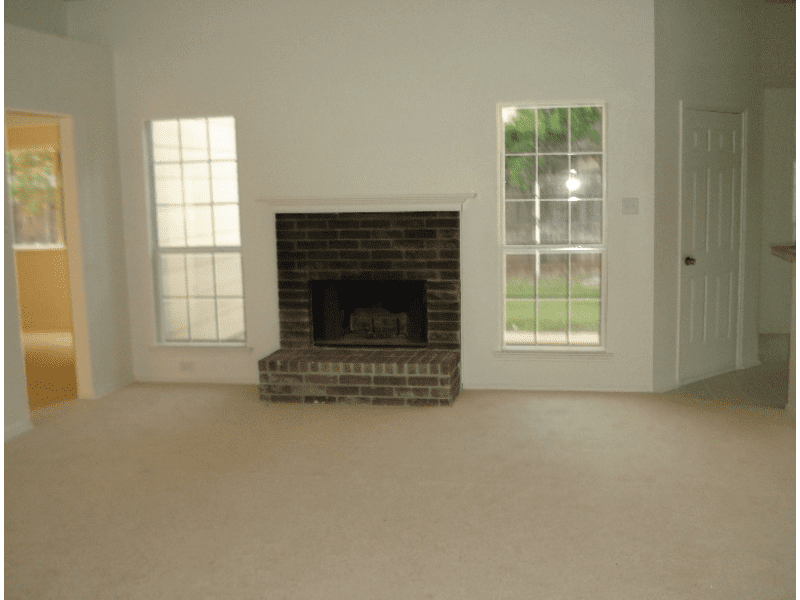 Empty living room with a brick fireplace and large windows.