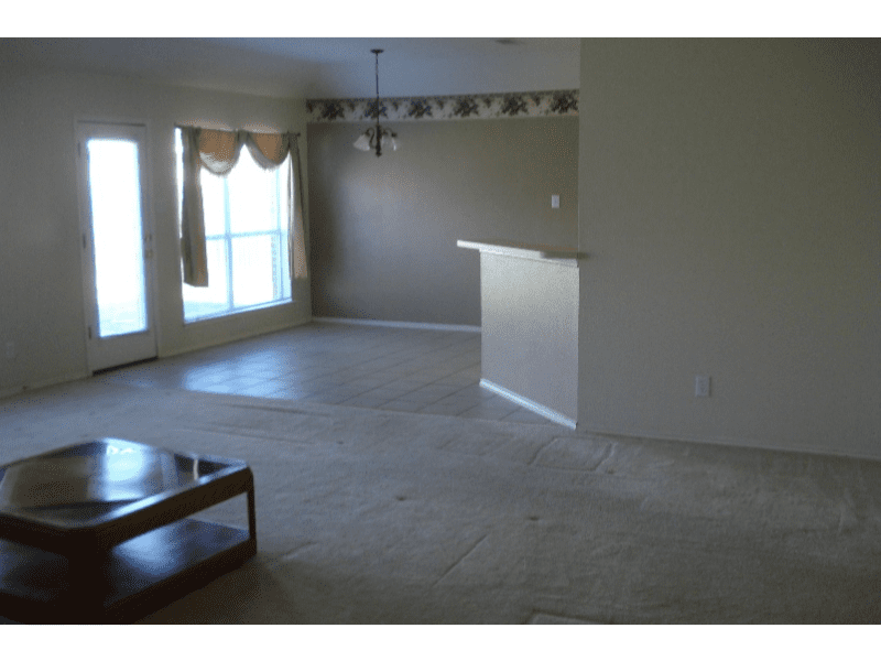 Empty living room with beige carpet and large windows.