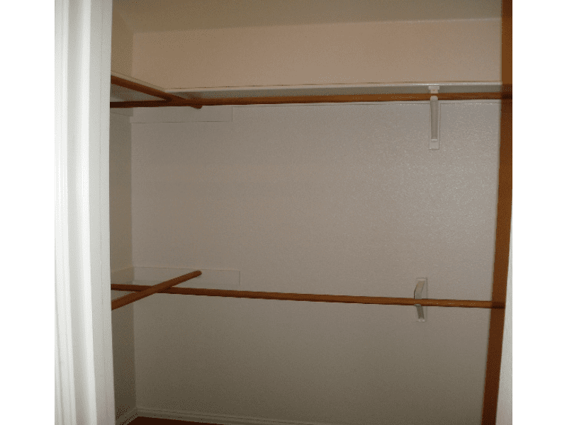 Empty walk-in closet with wooden hanging rods and shelves.