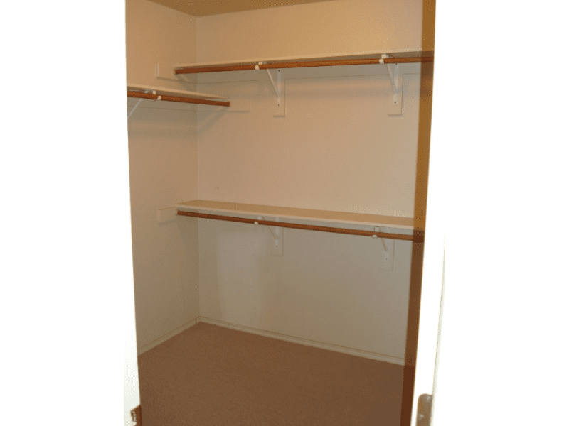 Empty walk-in closet with wooden shelves and hanging rods.