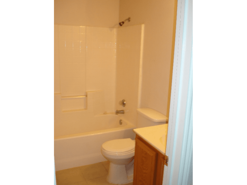 Clean bathroom with bathtub, toilet, and wooden cabinet.